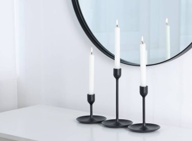 Beyaz duvarın yanında yanan mumlarla süslü şamdanlar ve kapalı alanda ayna, metin için yer