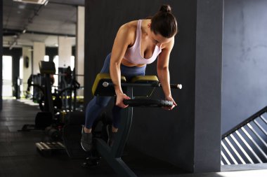 Spor salonundaki T-Bar sıra makinesinde ağırlık plakalı atletik kadın antrenmanı