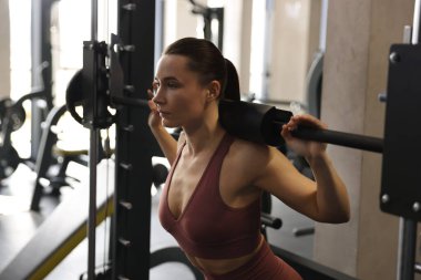 Spor salonunda Smith makinesinde halterli kadın antrenmanı