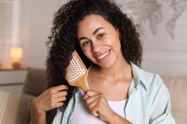 Gülümseyen genç bir kadın evde kıvırcık saçlarını tarıyor.