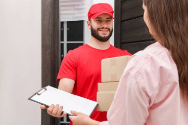 Paketlerle gülümseyen kurye kapalı alandaki alıcıya pano veriyor