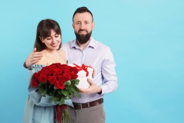 Kırmızı gülleri ve açık mavi arka planda hediye kutusu olan sevimli bir çift.