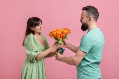 Adam pembe arka planda sevgili karısına bir buket güzel lale sunuyor.