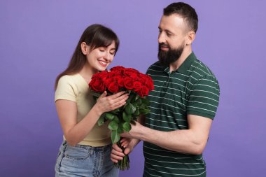 Adam mor arka planda sevgili karısına kırmızı güller sunuyor.