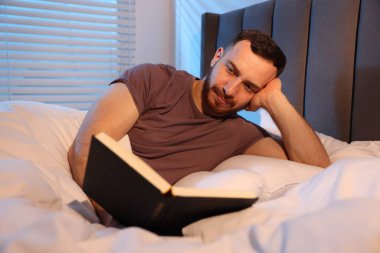 Genç adam evde yatakta kitap okumak