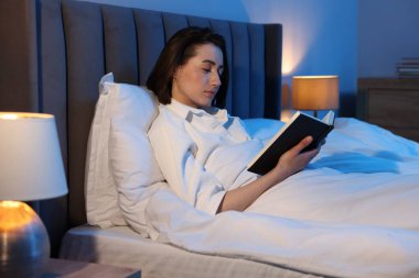 Evde yatakta kitap okuyan genç bir kadın.