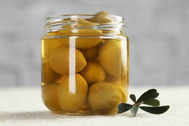 Kavanozda yeşil zeytin turşusu ve beyaz desenli masada yapraklar, yakın plan.