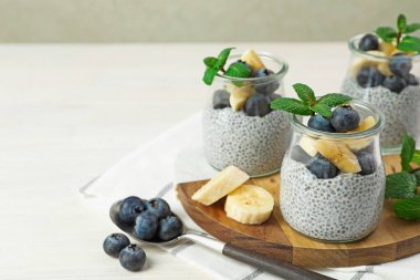 Yaban mersinli chia pudingi, muzlu ve naneli bardaklar ışıklı masada, yakın plan. Metin için boşluk