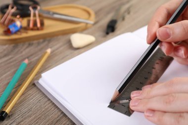 Ahşap masada cetvel ve kalemle çizim yapan kadın, yakın plan.