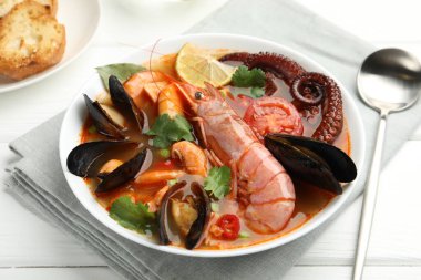 Beyaz ahşap masada servis edilen lezzetli deniz ürünleri çorbası, yakın plan.