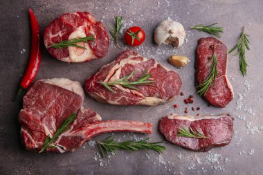 Flat lay composition with pieces of raw beef, salt, rosemary and products on brown textured table