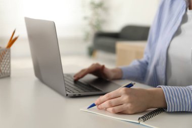 Beyaz masa içerisindeki çevrimiçi derste not alan bir kadın, yakın plan. Kendi kendine çalışma.