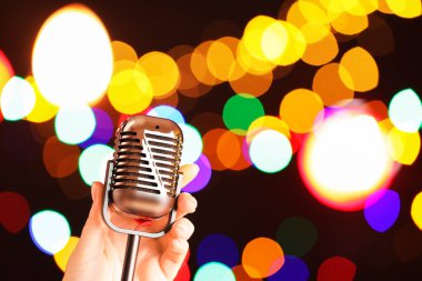 Karanlık arka planda, bulanık ışıkları, yakın çekimi ve mesaj için yeri olan klasik mikrofonu olan bir kadın. Bokeh etkisi