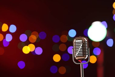 Koyu kırmızı arka planda, bulanık ışıkları olan klasik mikrofon, mesaj için yer. Müzik ekipmanları