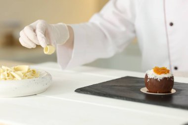 Mutfaktaki beyaz ahşap masada lezzetli bir tatlıyı dekore eden şekerci, yakın plan.