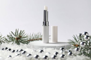 Nemlendirici dudak kremi, Noel dekorasyonu ve beyaz arka planda suni kar üzerindeki köknar ağacı dalları, yakın plan. Kış bakımı