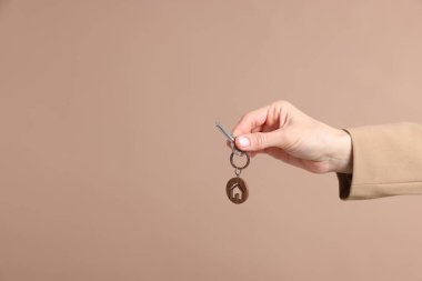 Emlakçının elinde anahtarlık bej arka planda ev şeklinde anahtarlık var. Yakın plan. Metin için boşluk