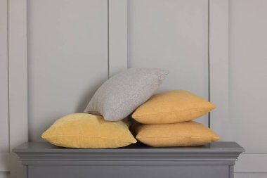 Gri duvarın yanındaki çekmecelerin üzerindeki yumuşak dekoratif yastıklar.