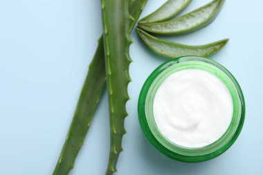 Aloe vera özütüyle nemlendirici krem ve açık mavi arkaplanda yapraklar, düz bir zemin.