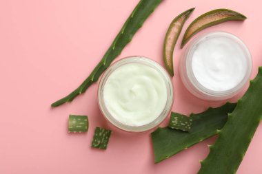 Aloe vera özütüyle nemlendirici krem ve pembe arkaplanda yapraklar, düz bir zemin.