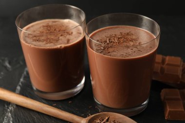 Lezzetli çikolatalı süt, siyah masanın üzerinde talaş ve parçalar, yakın plan.