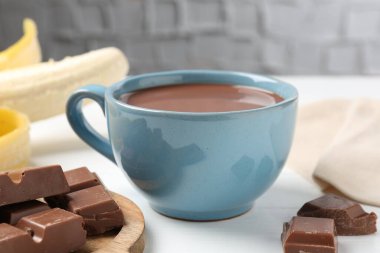 Lezzetli çikolatalı süt, parçalar ve muz beyaz ahşap masada, yakın plan.