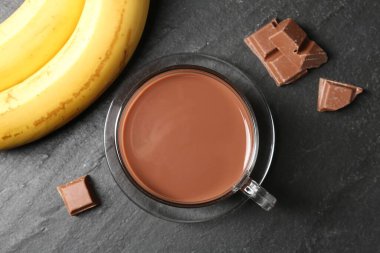 Cam bardakta çikolatalı süt, siyah masada parçalar ve muzlar.