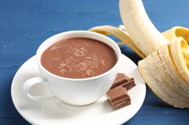 Lezzetli çikolatalı süt, parçalar ve muz mavi ahşap masada, yakın plan.