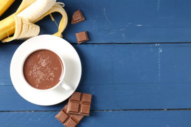 Lezzetli çikolatalı süt, parçalar ve muzlar mavi ahşap masada, düz uzanmış. Metin için boşluk