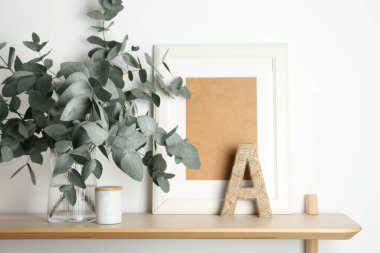 Vazodaki okaliptüs dalları ve beyaz duvarın yanındaki ahşap masa üzerindeki diğer dekorlar.