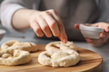 İçerideki masada pişmemiş krakerlere deniz tuzu ekleyen kadın, yakın plan.