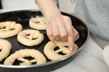 İçerideki masada pişmemiş krakerlere deniz tuzu ekleyen kadın, yakın plan.