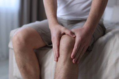 Evdeki yatakta diz ağrısı çeken bir adam, yakın plan.