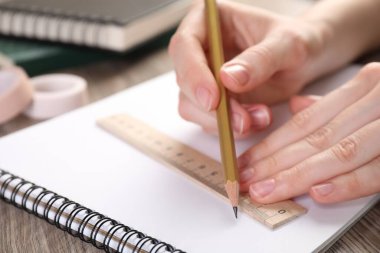 Ahşap masada cetvel ve kalemle çizim yapan kadın, yakın plan.