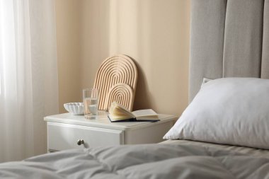 Yatağın yanında kitap, dekor ve bir bardak su olan komodin.