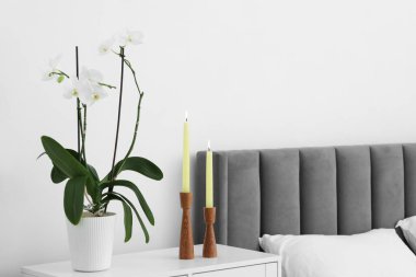 Yanan mumlarla süslü şamdanlar ve yatağın yanındaki komodinin yanında orkide çiçeği.