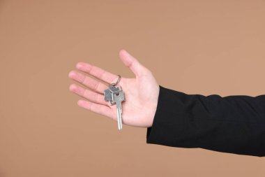 Emlakçının elinde anahtarlık bej arka planda ev şekilli anahtarlık, yakın plan.