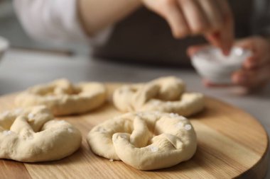 İçerideki masada pişmemiş krakerlere deniz tuzu ekleyen kadın, seçici bir odak noktası.