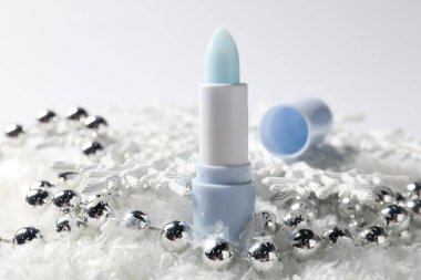 Nemlendirici dudak kremi ve yapay kar üzerindeki Noel süsü beyaz arka planda, yakın plan. Kış bakımı