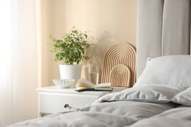 Yatağın yanında kitap, dekor ve bir bardak su olan komodin.