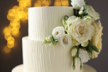 Gri arka planda çiçeklerle süslenmiş enfes düğün pastası. Bulanık ışıklar, yakın plan.