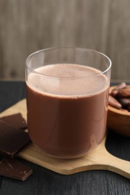 Lezzetli çikolatalı süt, barlar ve kakao çekirdekleri siyah ahşap masada, yakın plan.