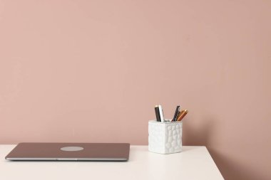 Laptop ve beyaz ofis masasındaki farklı kırtasiye malzemesi koyu bej arka planda