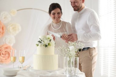 Evli çift evde bıçakla düğün pastası kesiyor, seçici bir odak noktası var.