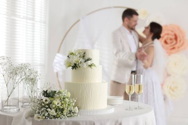 Mutlu evli çift içeride, düğün pastasına odaklanın, şampanya bardakları ve masa üzerindeki bukete.