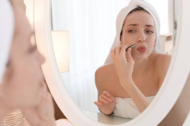 Güzel bir kadın evde aynanın yanında cımbızla bıyığını koparıyor.