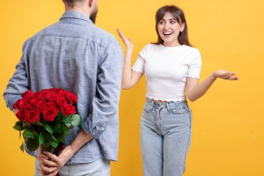 Adam turuncu arka planda sevgilisine kırmızı gül buketi saklıyor.