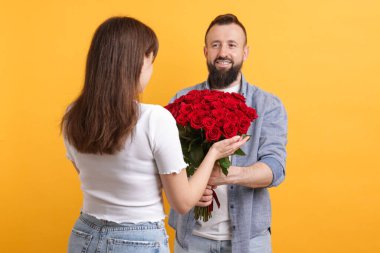 Adam turuncu arka planda sevgilisine kırmızı gül buketi sunuyor.