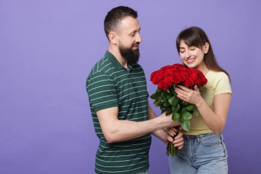 Erkek, sevdiği kadına mor arka planda kırmızı güller sunar. Mesaj için yer vardır.
