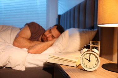 Evde uyuyan genç adam, çalar saate ve kitaba odaklan.